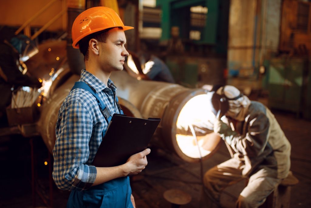 Master with notebook and welder on factory